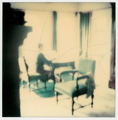 a blurry photo of a man sitting in a chair next to a piano and two chairs