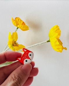 a hand holding a tiny red and white object with yellow flowers in the back ground