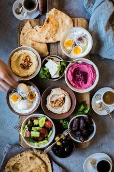 a table topped with bowls filled with different types of food next to cups of coffee