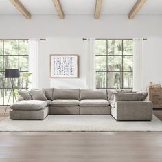 a living room with white walls and wood flooring, large sectional couch in front of two windows