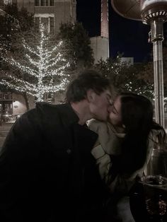 a man and woman kissing in front of a christmas tree with lights on the street