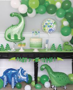 a dinosaur birthday party with balloons, cake and decorations on the table in front of it