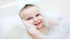 a baby smiles while sitting in a bathtub with foam on it's head