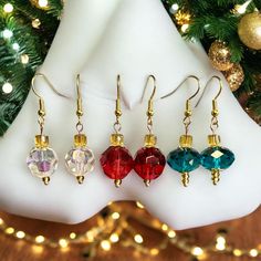 four different colored glass bead earrings hanging from gold earwires next to a christmas tree