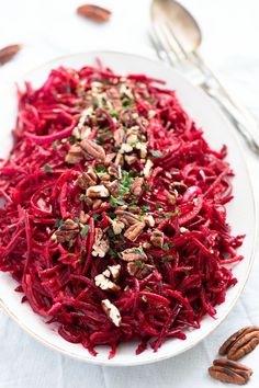 a white plate topped with beet slaw and pecans next to silverware