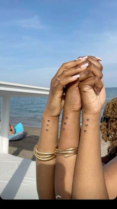 two women with matching tattoos on their arms holding each other's hands in front of the ocean