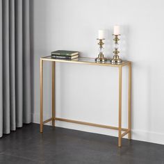 a gold console table with two candles and books on it in front of a window