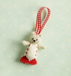 a white stuffed animal hanging from a red and white christmas ornament on a polka dot background