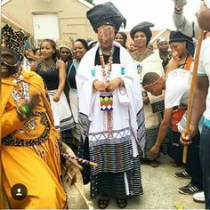 a group of people standing next to each other in front of a building and one person wearing an african headdress