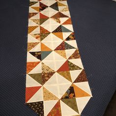 a quilted table runner on top of a blue mat with an orange and white design