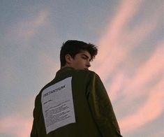 a young man wearing a green jacket and standing in front of the sky with his back turned to the camera