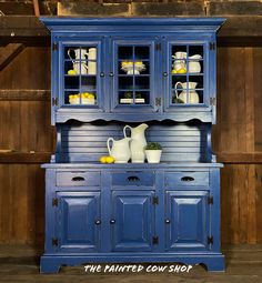 a blue china cabinet with glass doors and yellow dishes on it's top shelf