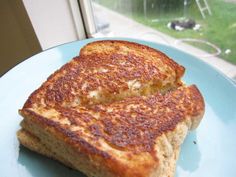 two pieces of grilled cheese on a blue plate near a window with a dog in the background