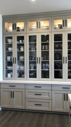 a kitchen with white cabinets and glass doors on the front, and wood flooring