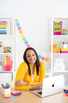 a woman sitting at a desk with a laptop in front of her and colorful confetti on the wall behind her