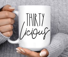 a woman holding a white coffee mug with the words thirty vicious on it in black ink