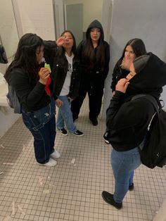 four women standing in a bathroom looking at their cell phones and taking pictures with each other