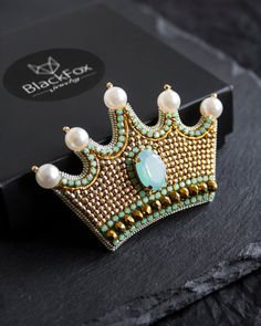 a gold and blue tiara with pearls on it sitting next to a black box