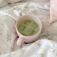 a cup filled with green liquid sitting on top of a white bed covered in floral sheets