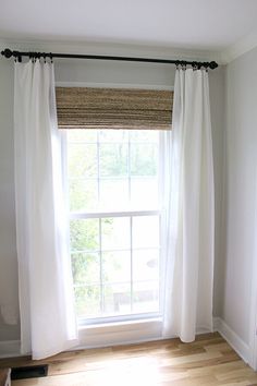 an empty room with white curtains and wood flooring on either side of the window