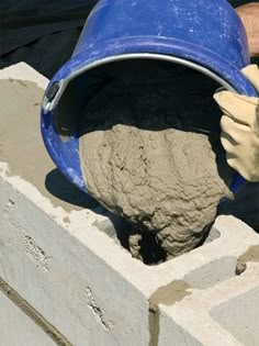 someone is pouring cement into a blue bucket