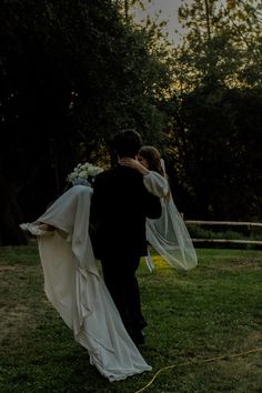 the bride and groom are walking through the field at sunset with their veil blowing in the wind