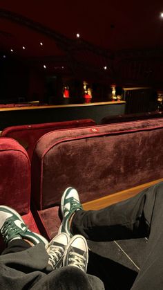 someone is sitting in an empty theater with their feet up on the seats and they are wearing green sneakers