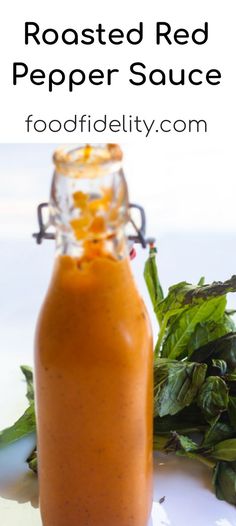 a glass bottle filled with red pepper sauce sitting next to some green leaves on a white surface