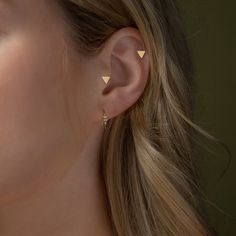 a close up of a woman's ear with two small gold triangles on it