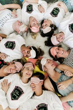 a group of people laying on top of each other wearing white shirts and covering their eyes