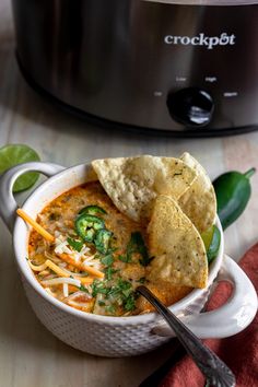 a bowl of soup with tortilla chips in front of an electric crockpot