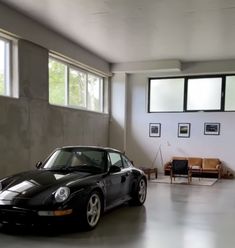 a black porsche parked in a garage next to two couches and windows with pictures on the wall