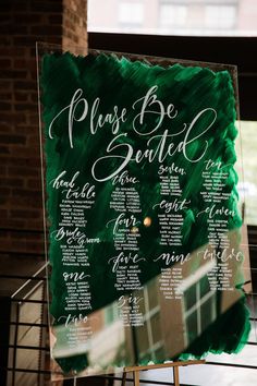 a green and white wedding seating chart on a wooden easel in front of a window