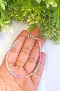 a hand holding a small bracelet with beads on it and flowers in the back ground