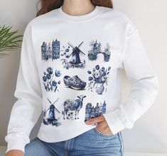 This delft blue art sweatshirt featuring tulips and windmills is the perfect gift for those who love everything Dutch and have a soft spot for Amsterdam. The cozy medium-heavy fabric blend of cotton and polyester provides warmth during colder months, while the classic fit and crew neckline offer a comfortable and stylish look. Ideal for anyone who appreciates Holland's culture and wants to showcase their love for Dutch art and heritage. Perfect for gifting during Dutch-themed parties, tulip festivals, or as a souvenir from a trip to Amsterdam. Product features - Ethically sourced fabric blend of 50% cotton and 50% polyester for coziness and durability - No side seams for reduced fabric waste and a cleaner look - Ribbed collar with seam for elasticity and shape retention - Double-needle sti Dutch Tulips, Dutch Tulip, Gift For Traveler, Art Sweatshirt, Dutch Art, Tulip Festival, Soft Spot, Delft Blue, Blue Art