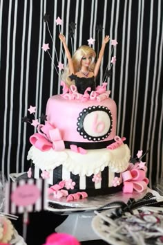 a barbie doll is sitting on top of a pink and black birthday cake with stars