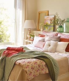 a bed with pink and green sheets in a bedroom next to a window filled with flowers