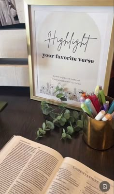 an open book sitting on top of a table next to a vase filled with pens and pencils