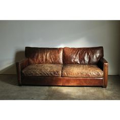 a brown leather couch sitting on top of a cement floor next to a white wall