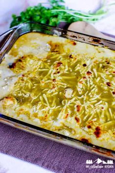 a casserole dish with cheese and green sauce in it on a purple cloth