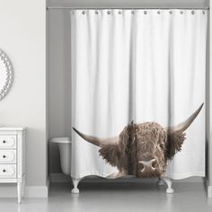 a shower curtain with an image of a bull's head on it, in front of a white dresser and mirror