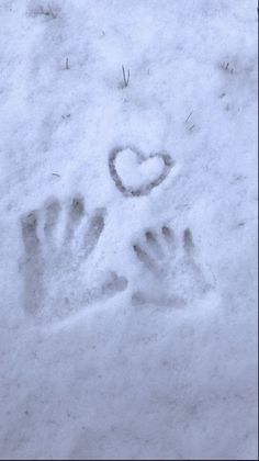 a person's hand and foot prints in the snow with a heart on it