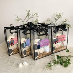 three clear bags with black bows are sitting on a table next to white flowers and greenery