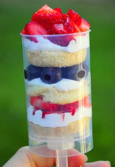 a person holding up a plastic cup with strawberries and cream in it on the grass