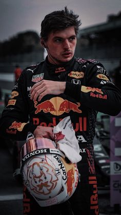 a man holding a helmet on top of his shoulder and wearing a red bull uniform