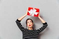 a woman holding up a red box with a white bow on it's head