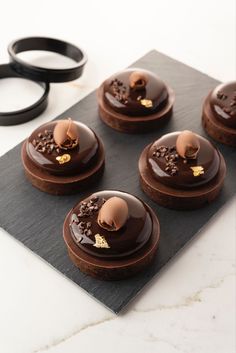 four chocolate desserts are sitting on a black plate with scissors next to them and some other items