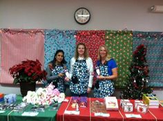 three women in aprons stand behind a table with christmas decorations and gifts on it