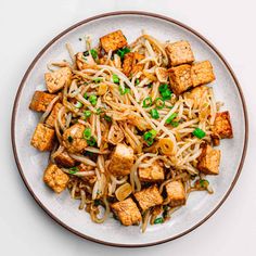 a plate with noodles, tofu and peas on it is sitting on a white surface