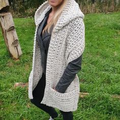 a woman standing in the grass wearing a white crochet cardigan and black leggings